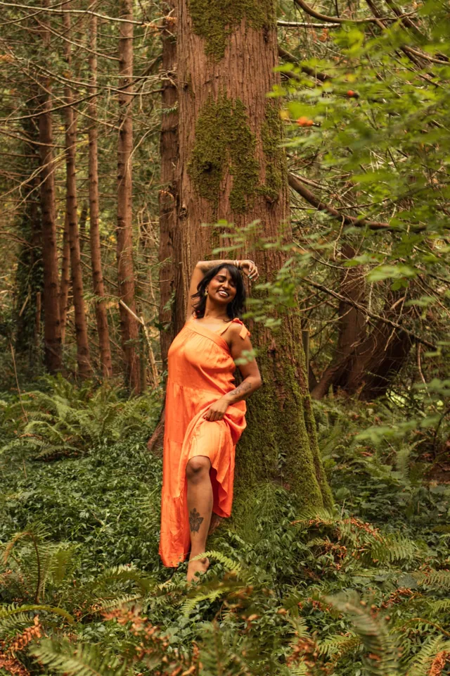 A woman in an orange dress leaning against a big tree